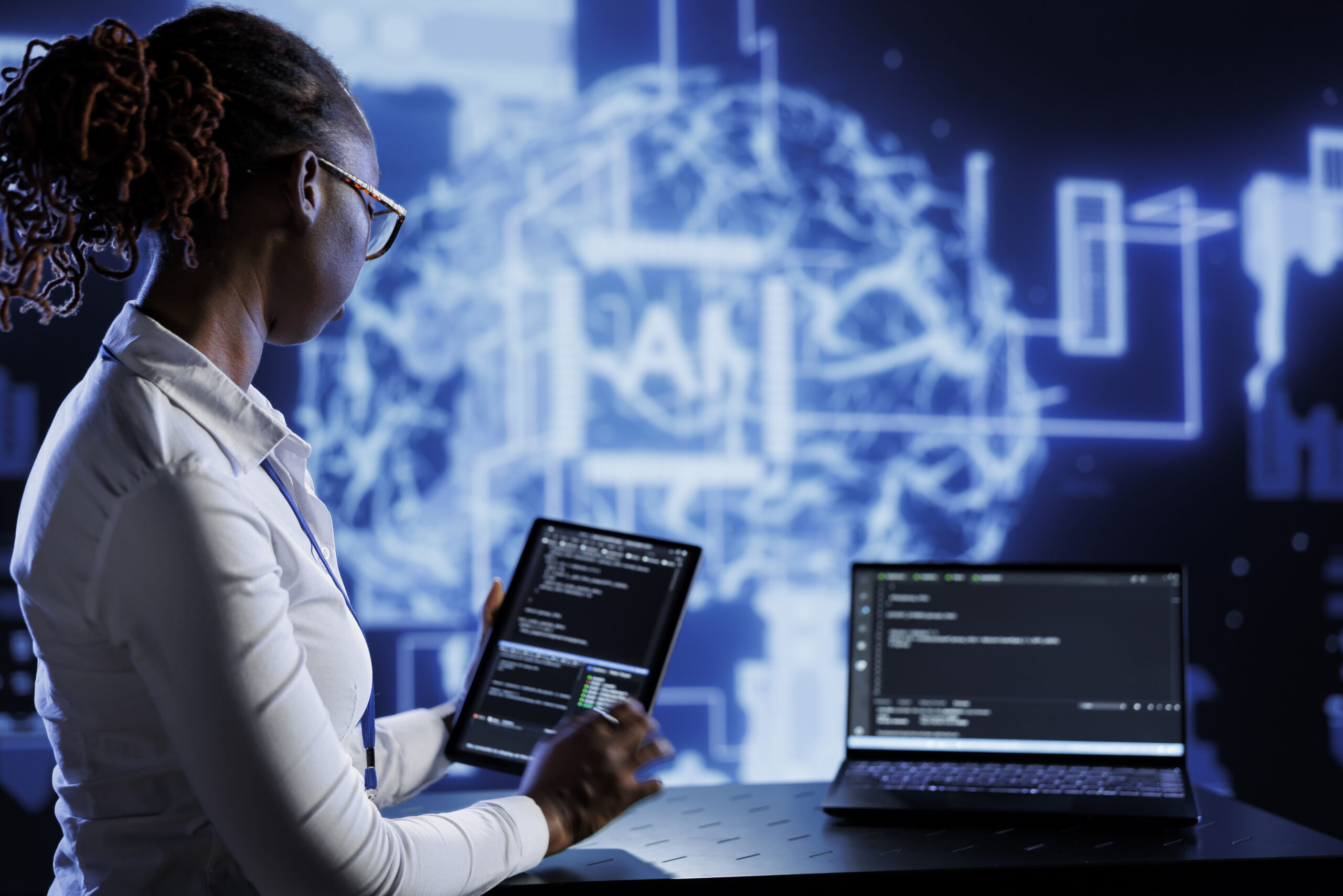 Computer scientist updates neural networks made of interconnected nodes, writing intricate binary code scripts on tablet and laptop. Server room expert uses programming to upgrade AI simulation model